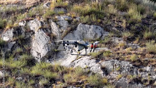 Drone Spraying Vegetation with Rocky Cliff Hillside in background