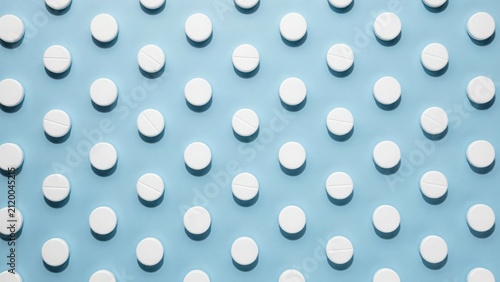 Uniform grid pattern of small white medicinal pills on soft blue background with health care medicine pharmacy background