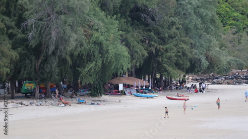 The image depicts a beach scene with a wide stretch of sand and several people scattered across the area, some walking and others lounging