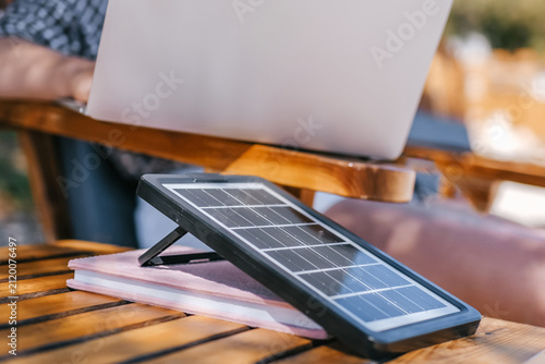 Foto Digital nomad working on laptop at beach lounge, portable solar panel charger on table, remote work vacation concept, sustainable travel, work from anywhere lifestyle