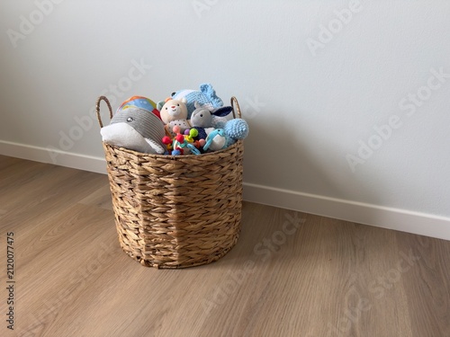 Obraz na płótnie Wicker basket filled with colorful plush soft toys stands on wooden floor near white wall