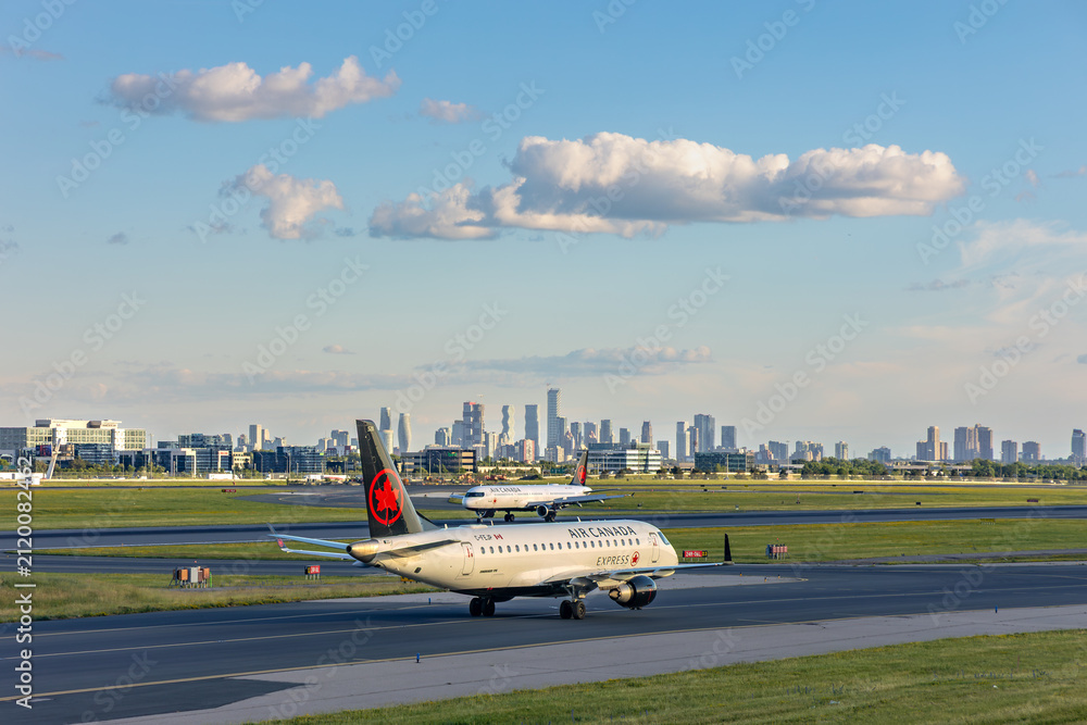 Fototapeta premium Two Air Canada passenger aircraft taxi at Toronto Pearson airport before the skyline.