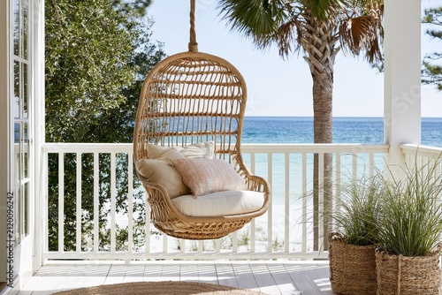 A hanging chair on a coastal cottage porch, complemented by beach grasses nearby and uncluttered center area and elegant symmetry.