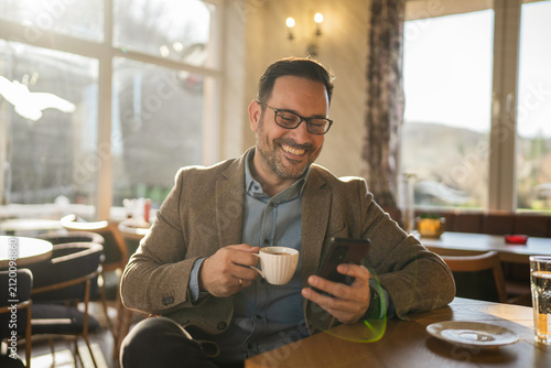 Happy man relaxing and using phone in a cafe
