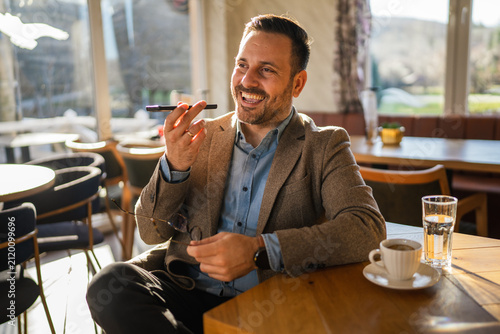 Bild auf Leinwand Smiling man using smart phone speakerphone for voice message in cafe