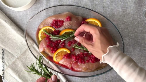 preparing chicken fillet for baking with rosemary sprigs red currants and orange slices creating fresh culinary composition concept of healthy cooking food styling recipes and gastronomy