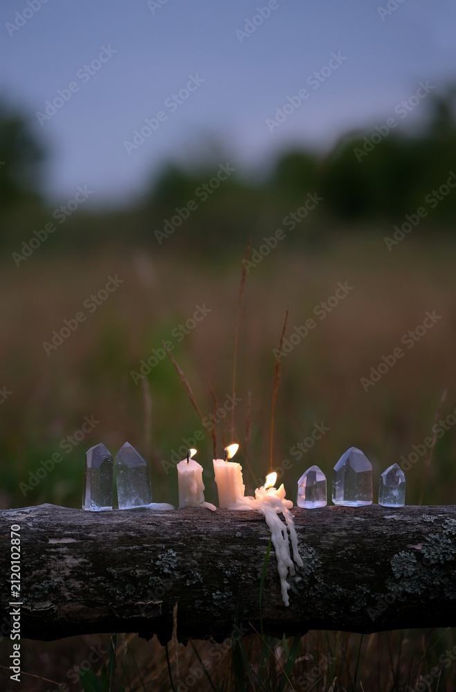 Fototapeta premium clear quartz crystals and burning candles outdoor, abstract dark natural evening background. Witchcraft, Esoteric spiritual ritual, practical magic for life balance, cleansing aura. soft focus