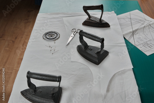 Mesa con patrón de costura, planchas antiguas de hierro, tijeras, alfileres y tela
