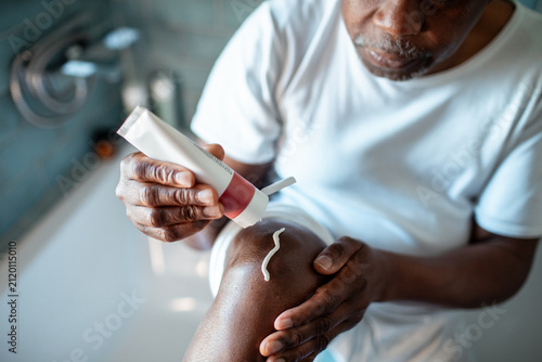 Senior man applying topical cream to knee at home