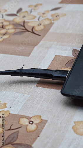 Damaged black cable with electrical tape connecting to a device, showing a makeshift repair on a patterned tablecloth