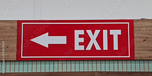 Red sign with white EXIT text and a left pointing arrow providing clear directional guidance for egress