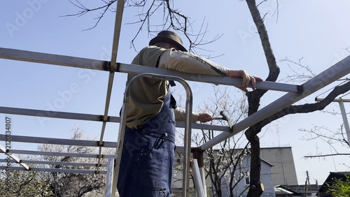 Foto Male laborer uses a hammer to strike welded metal joints on carport frame