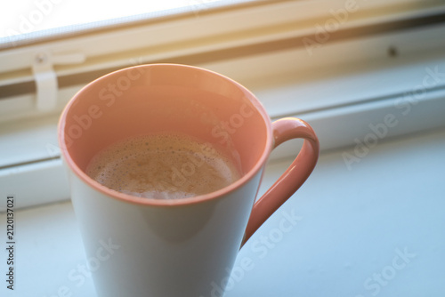 Close-up of a ceramic mug filled with fresh hot coffee placed near a bright window.