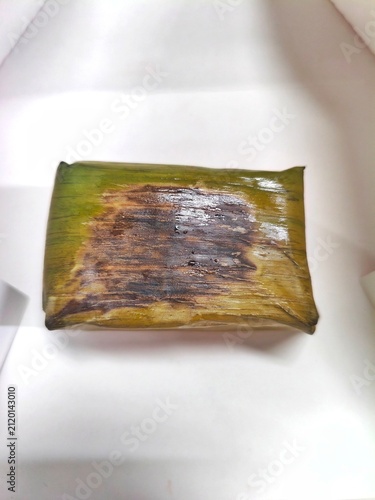a traditional Indonesian rice roll with chicken filling in banana leaves inside a white box, close-up angle