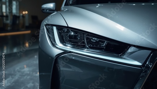 Detailed view of a contemporary silver car's headlights. Luxury vehicle in a showroom with LED lighting.