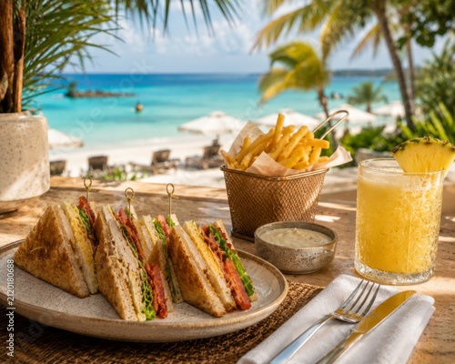Fresh club sandwich with crispy fries and tropical pineapple drink served at a beachfront restaurant overlooking turquoise ocean. Relaxed summer vacation dining concept.