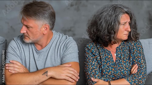 A middle-aged couple sits with arms crossed, displaying visible tension, disapproval, and emotional distance during a.