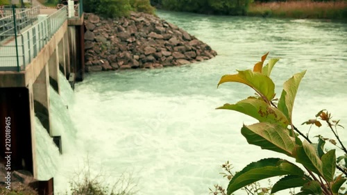 Small hydroelectric station on the Drac River in France with flowing water, concrete floodgates and surrounding vegetation. Renewable energy, hydropower and green electricity concept