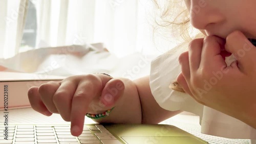 Close-up of a young child hesitating while using a laptop keyboard at home. Novice user, digital learning, uncertainty, online education and childhood technology concept