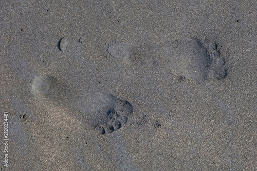Fotografie Close-up of barefoot footprints impressed in dark grey beach sand