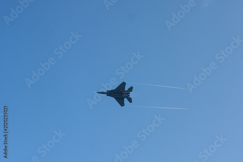 Quadro su tela Bottom-up view of a military fighter jet flying through a clear blue sky with wi