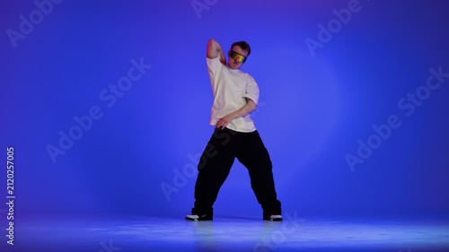 Hip hop dancer performing rhythmic freestyle on blue studio background