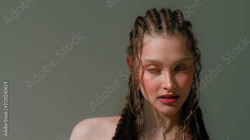 Calm young woman with braided hair in soft studio light, turning gently through elegant beauty pose