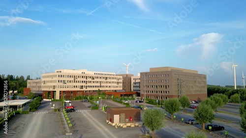 Aerial view of a modern corporate headquarters with wind turbines, showcasing sustainability and green energy. Cinematic drone establishing shot of a business park campus.