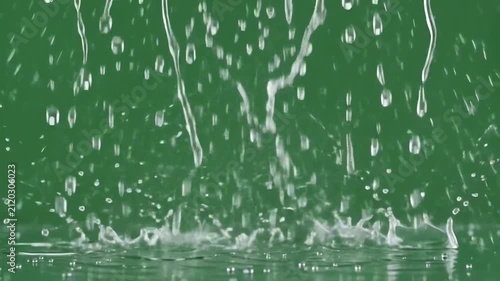 Realistic rain drops falling and splashing against a bright green screen chroma key background for video overlay effects