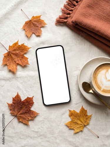 Autumn smartphone mockup with blank screen on a linen background surrounded by fall leaves, coffee cup and cozy throw with copy space