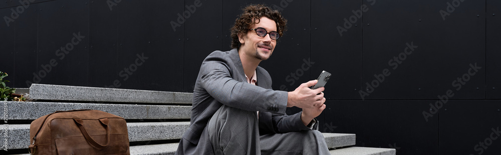 Obraz premium Handsome man with curly hair dressed elegantly enjoys a moment on the street steps