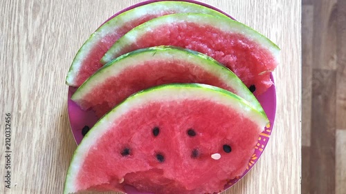 Stacked fresh watermelon slices with red flesh and black seeds on wooden surface, summer fruit.