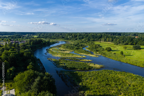 Fotografía Aerial view of Venta River near Kuldiga, Latvia shows braided channels, vegetated islands, hay bales to the right, and forest to the horizon on a clear summer day