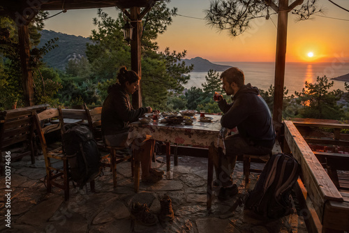 Two travelers sharing dinner on a rustic sea-view terrace at sunset. generative AI