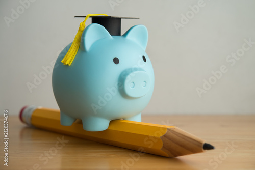 Piggy bank with mortarboard riding pencil on wooden table. Education, money savings and financial planning for education in university, college or study abroad, scholarship and so on concept.
