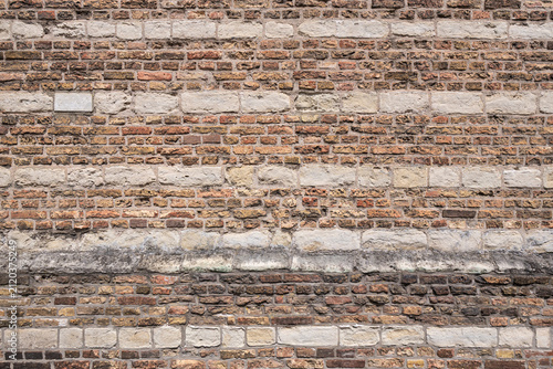 old masonry wall featuring alternating horizontal bands of reddish-brown clay bricks and lighter-colored ashlar stone blocks