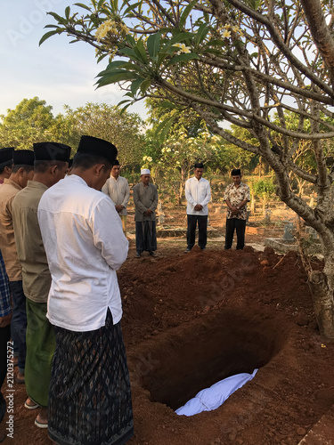 Indonesian Muslim community gathered around an open grave during burial rites. generative AI