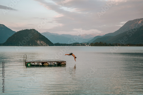 teenager diving from floating dock into calm alpine lake at dusk