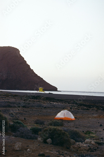 A lone tent set against a vast volcanic landscape at sunset.
