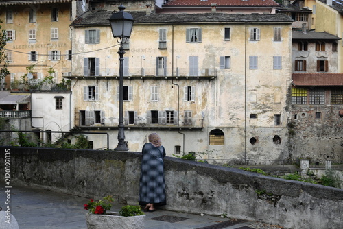 Elderly woman standing on a bridge in front of historic buildings in Italy