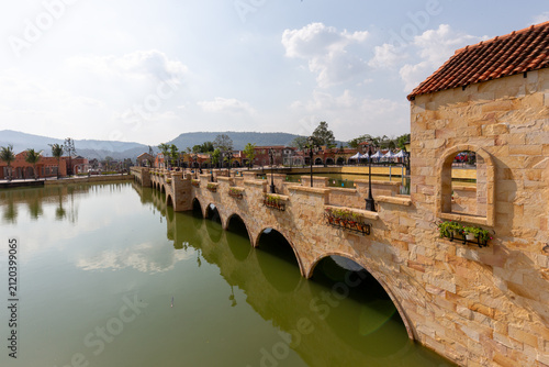 Fotografie Tuscan-style stone arch bridge built over a green lake with European architectur