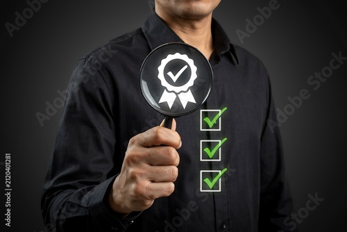 Professional man holding magnifying glass over quality assurance checkmark symbol in studio