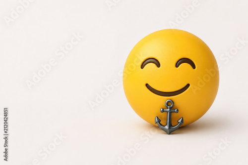 Smiling yellow face rests behind a metal anchor. Space for text.
