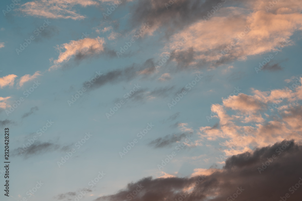 Fototapeta premium Soft blue evening sky filled with warm peach cloud bands and darker drifting layers, creating calm yet dramatic sunset atmosphere with open negative space, layered texture, and natural light