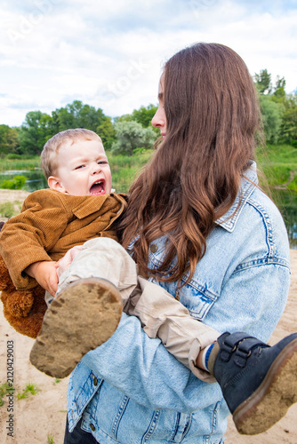 crying toddler boy held by mother during outdoor walk in park