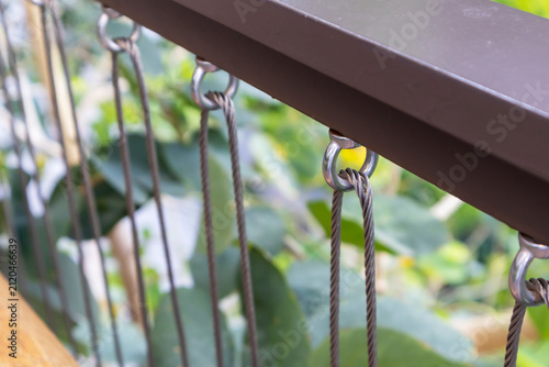 Circular steel bars with steel cables attached, used as a railing or safety fence in an outdoor garden.