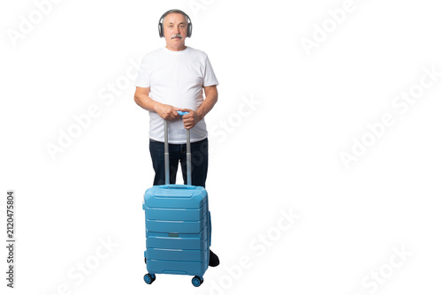 Cuadro en lienzo Senior traveler wearing wireless headphones while standing with a rolling suitcase