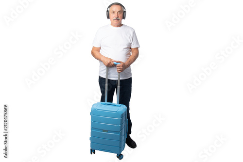 Cuadro en lienzo Senior traveler wearing wireless headphones while standing with a rolling suitcase