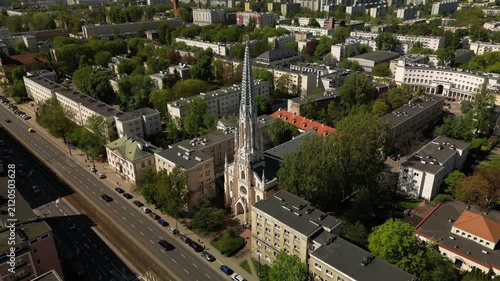 Drone footage of the neo-Gothic Evangelical Reformed Church in Warsaw, showing its tall spire, historic facade, city blocks and sunny urban setting.