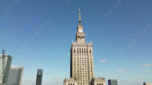 Drone footage of the Palace of Culture and Science in Warsaw, showing its historic tower, clock facade, surrounding streets and sunny city atmosphere